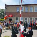 Strażacy wieszający flagę Polski oraz uczestnicy jubileuszu